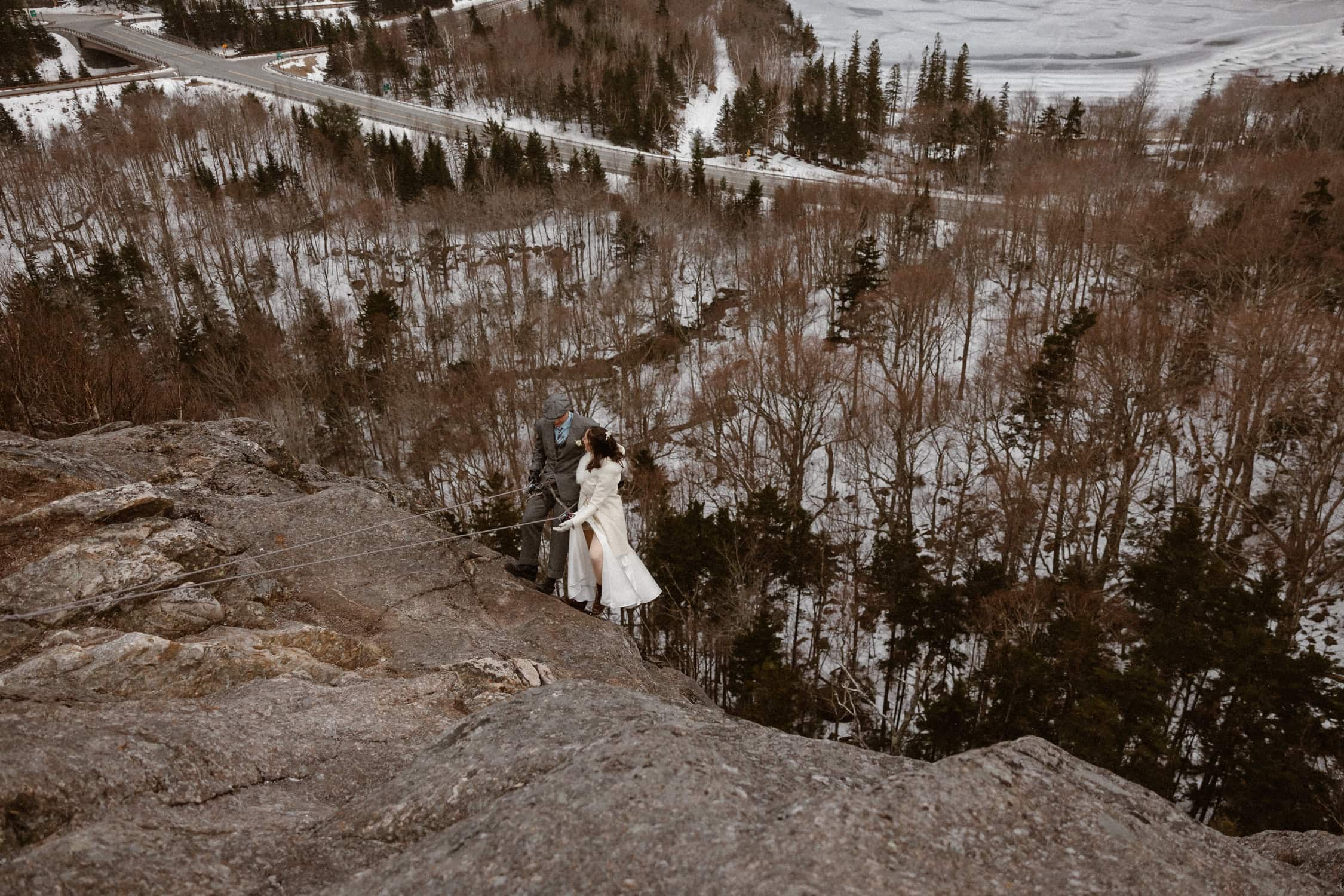 A couple rappelling down Artist's Bluff on their elopement day, standing side by side on the side of the cliff.