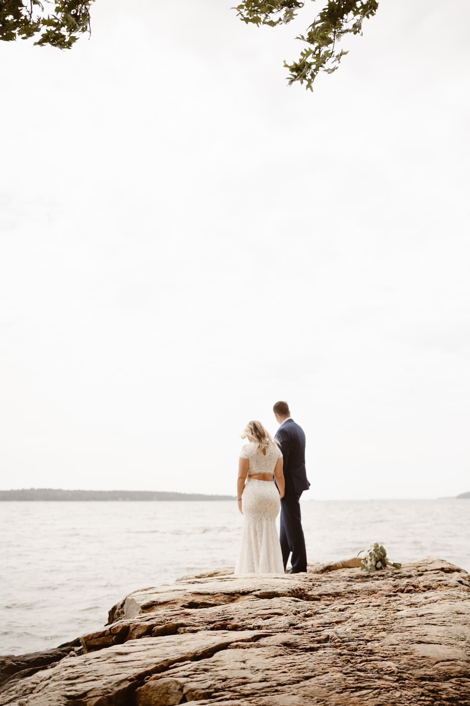 A couple standing on a rocky outcropping in Freeport Maine. They are wearing their wedding attire after their elopement ceremony.