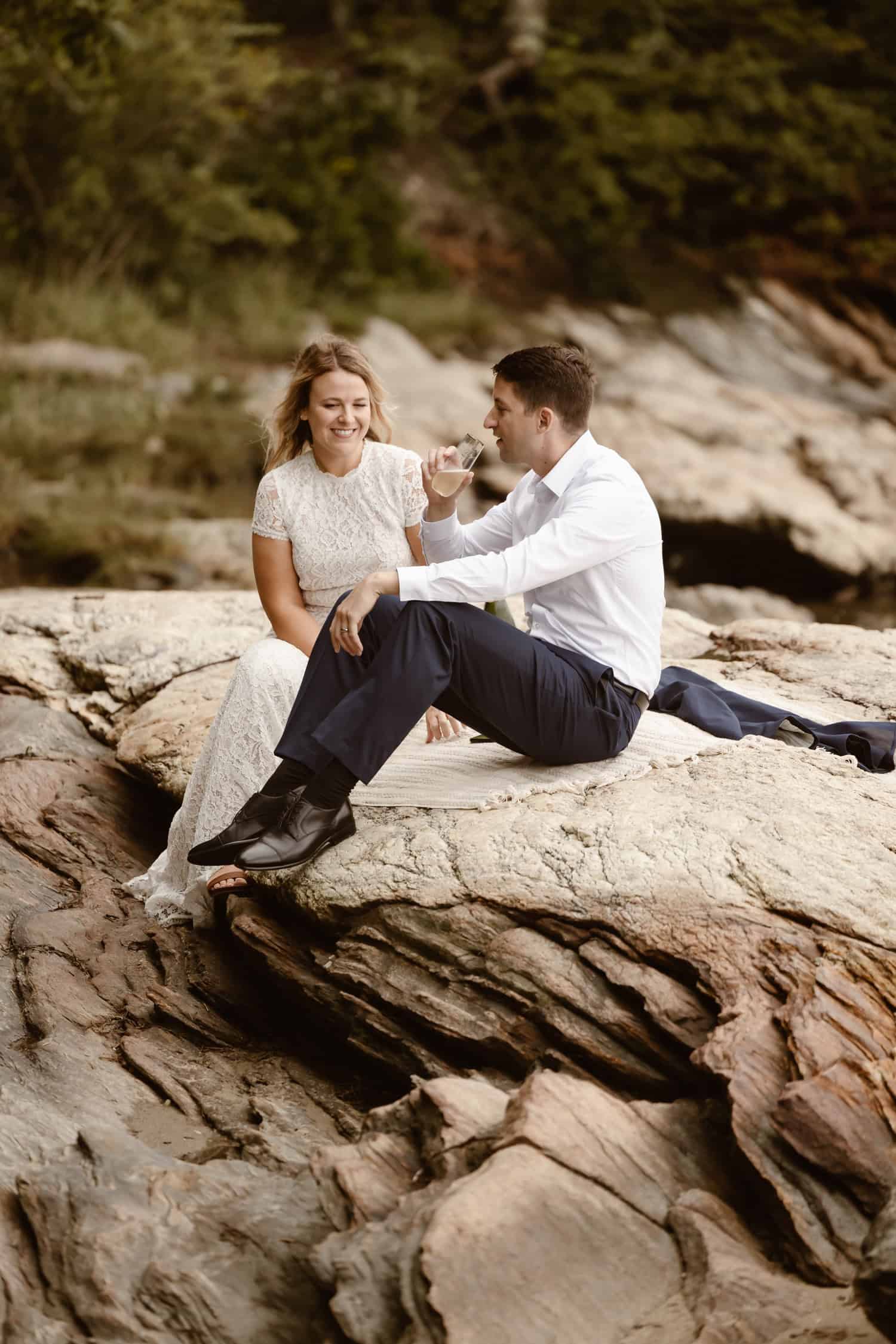 A couple sitting on a rock, enjoying a glass of champagne to celebrate their elopement in Freeport.