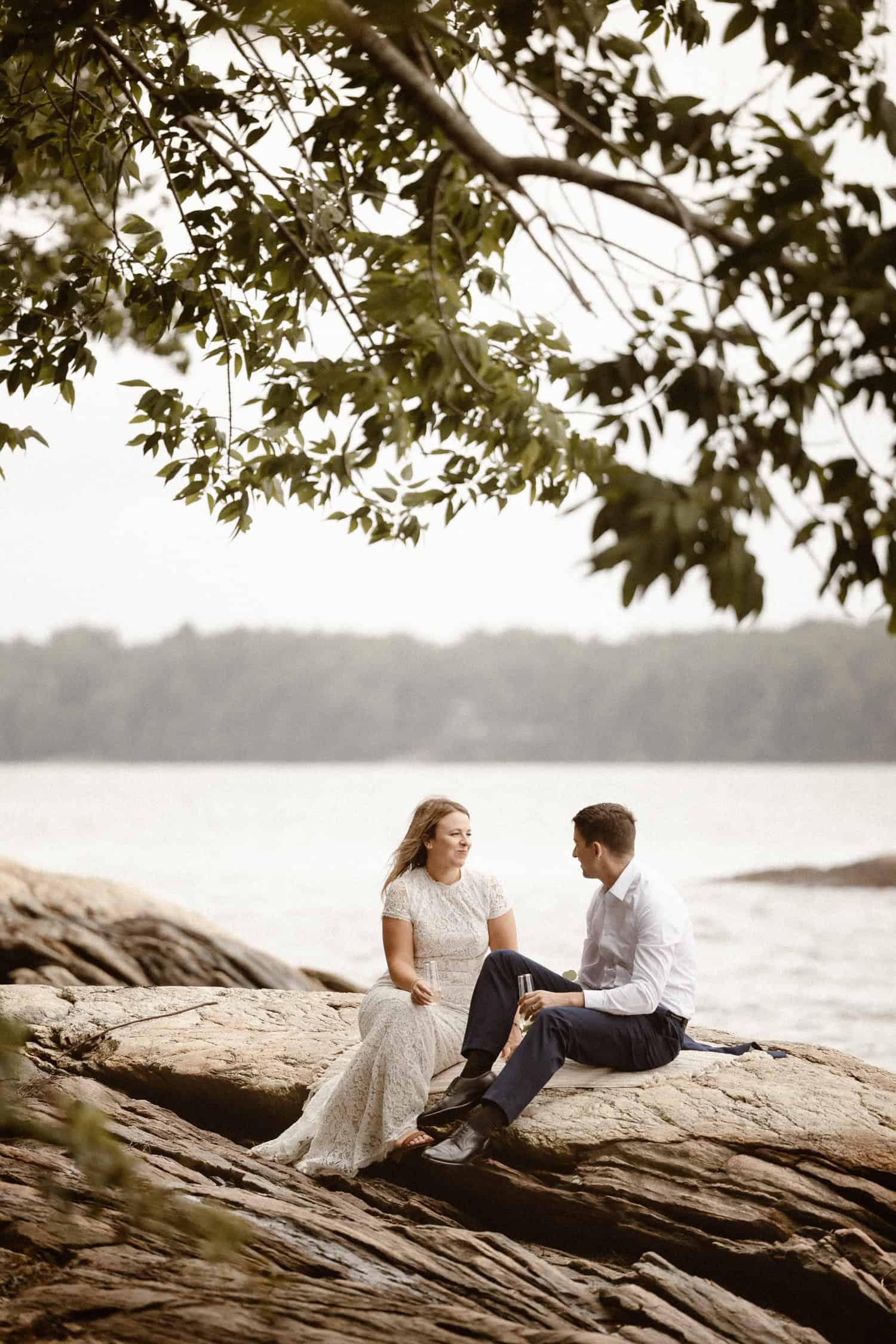 A couple sitting on a rock, drinking champagne after their elopement ceremony in Freeport.