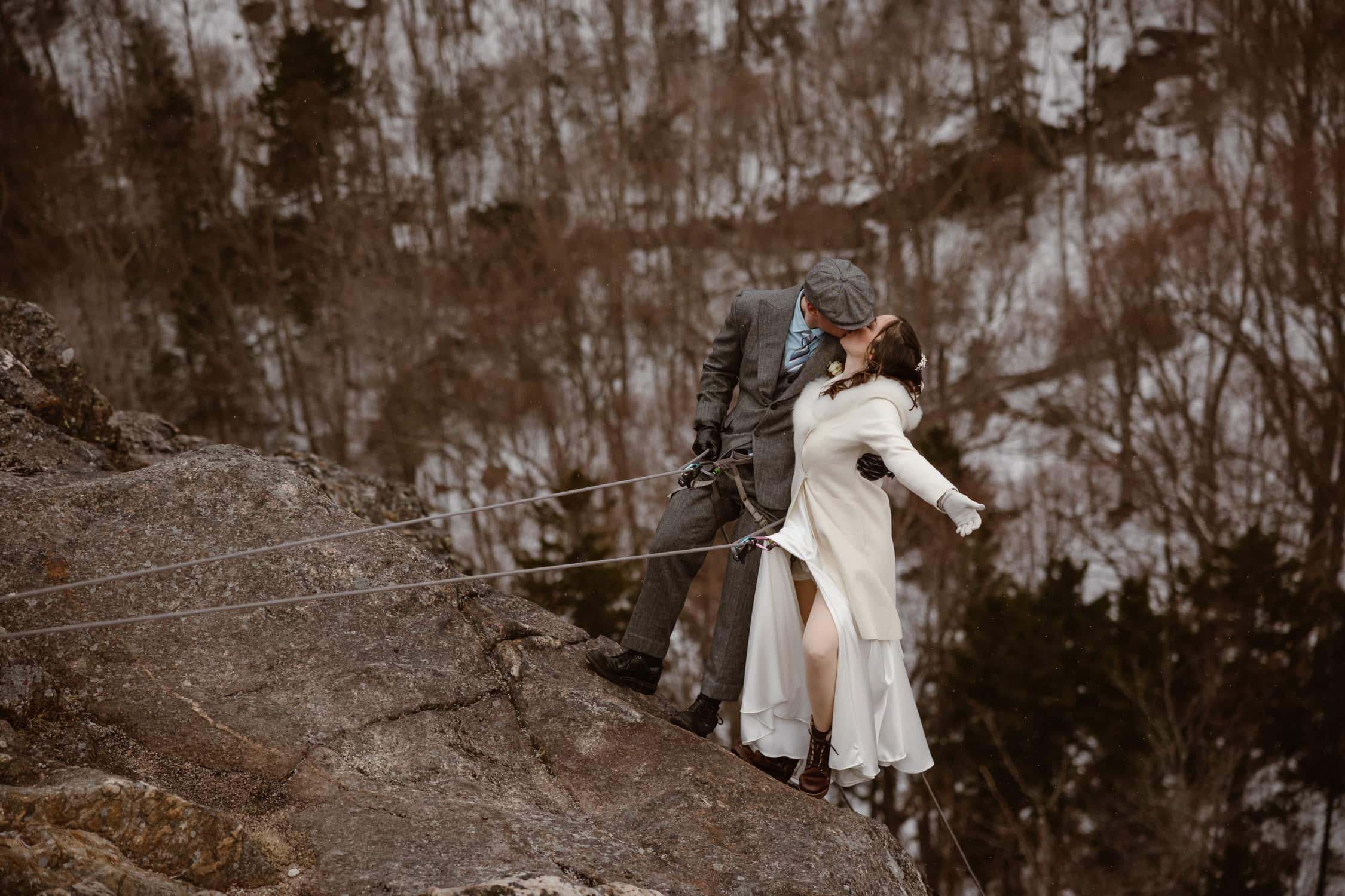 A bride and groom kissing, while clipped in after rappelling down Artist's Bluff.