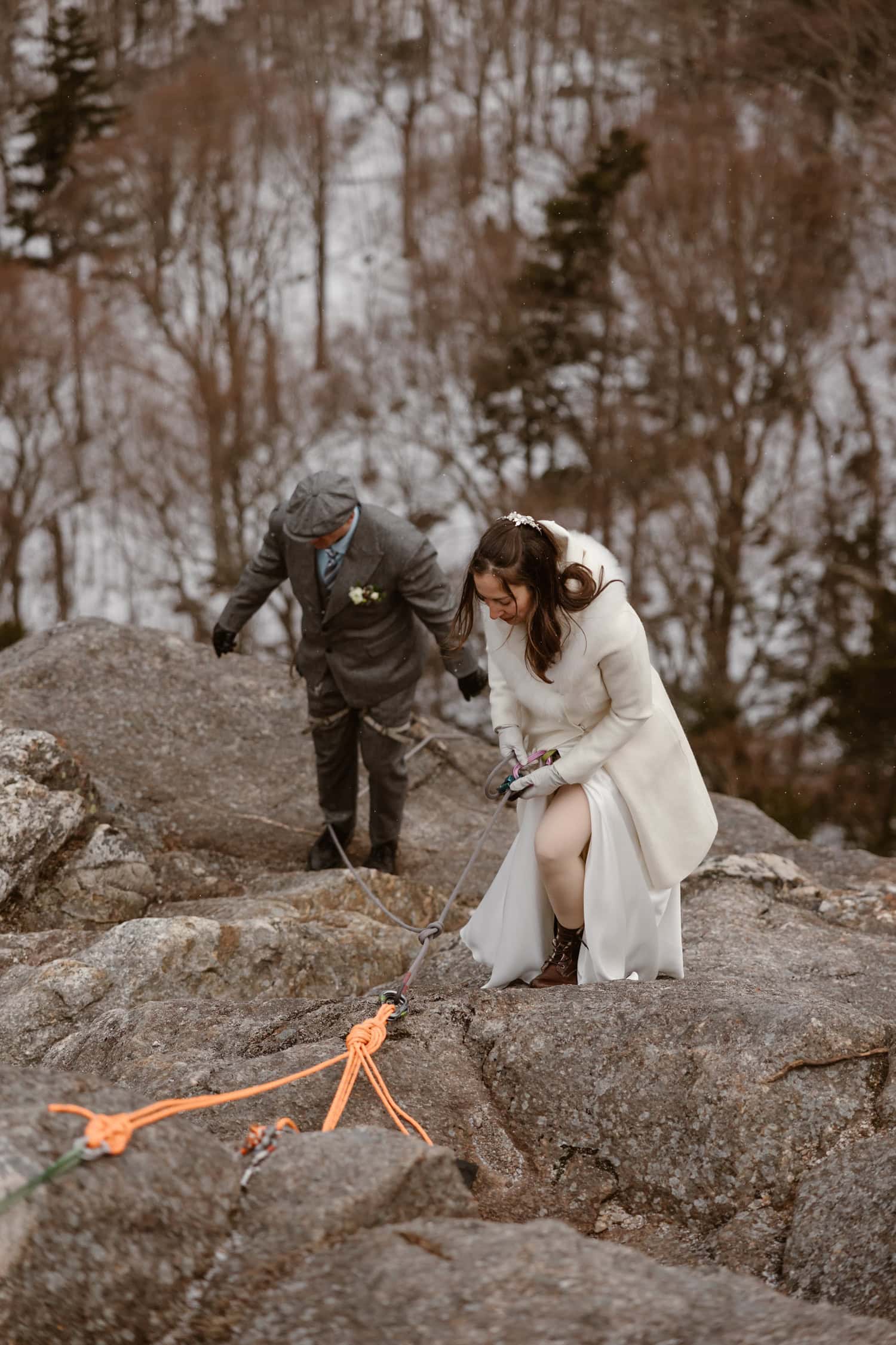 A bride and groom rappeling down a rock face, wearing their elopement attire.