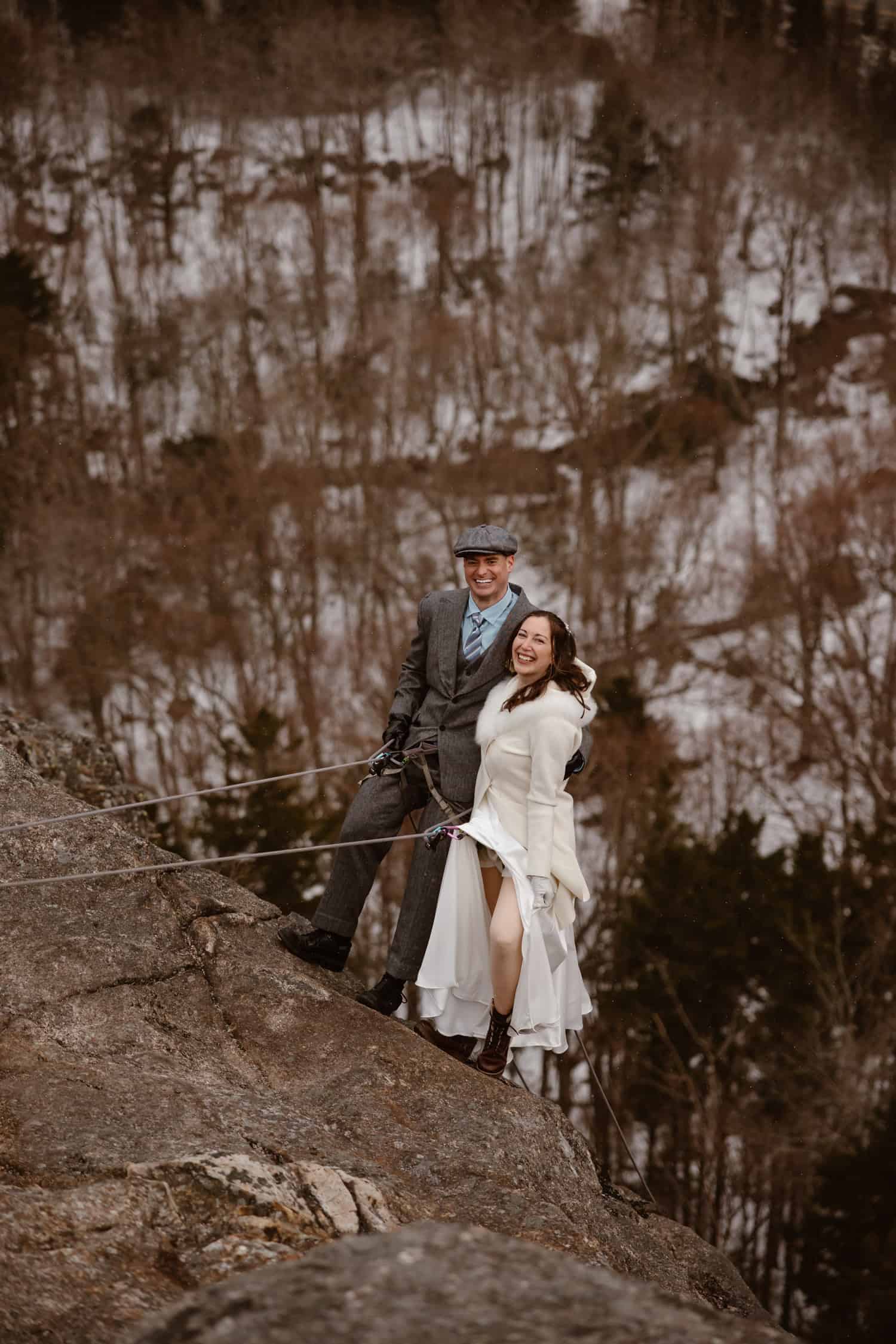 A couple rappelling down Artist's Bluff on their elopement day, standing side by side on the side of the cliff.