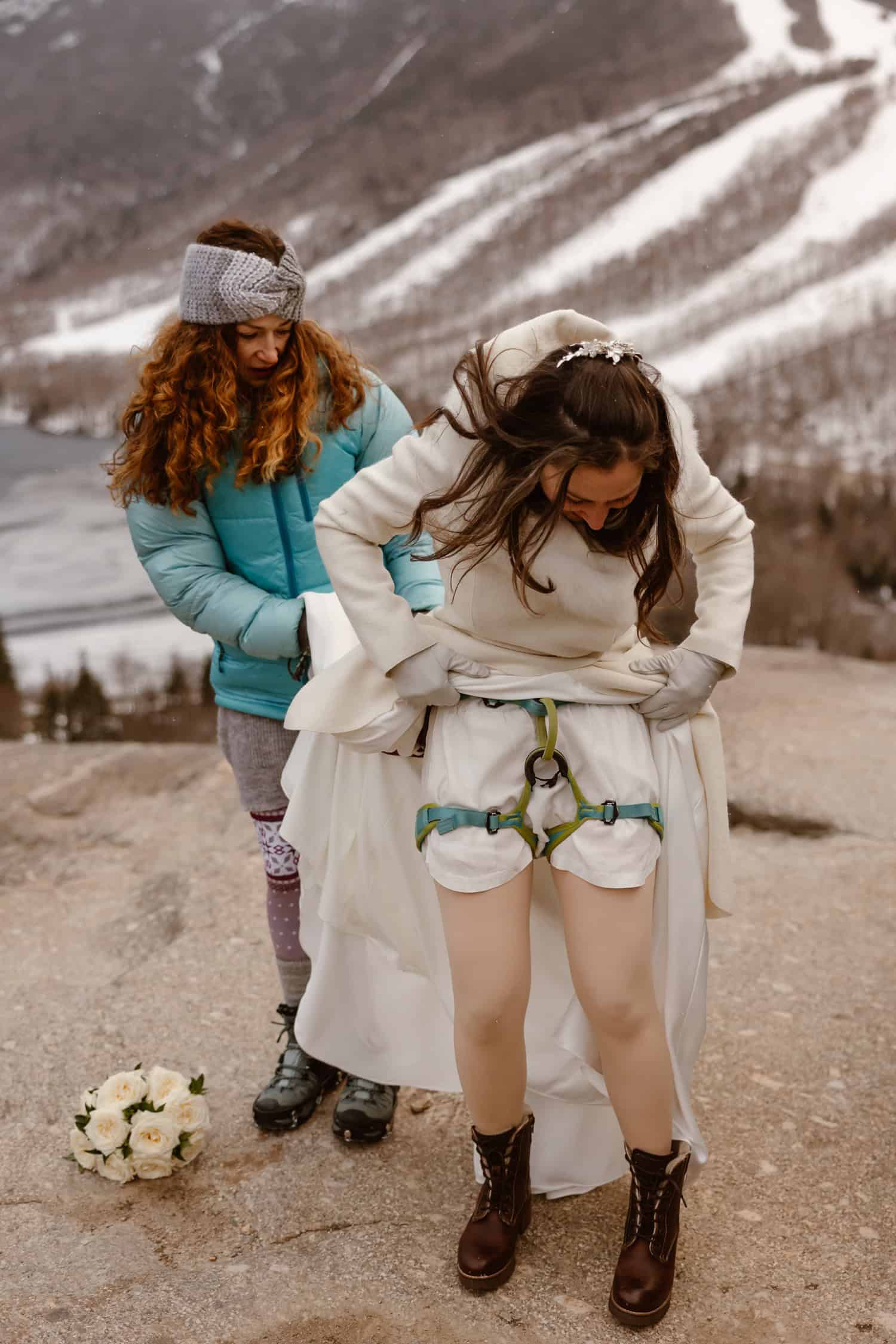 A bride getting ready for her rappel elopement, putting the harness on under her dress.